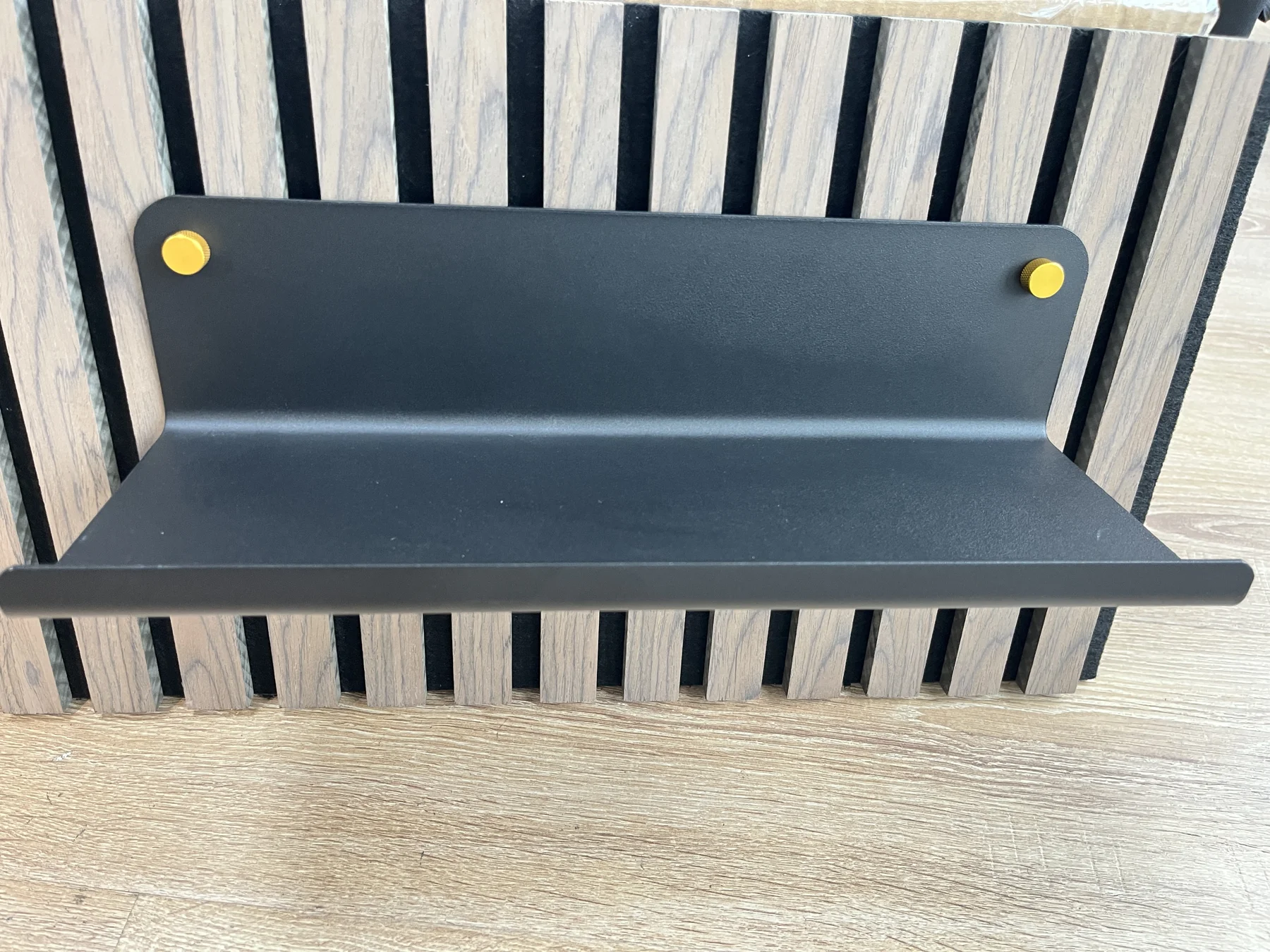 Black shelf with gold-coloured visible fasteners on a small sample slat panel